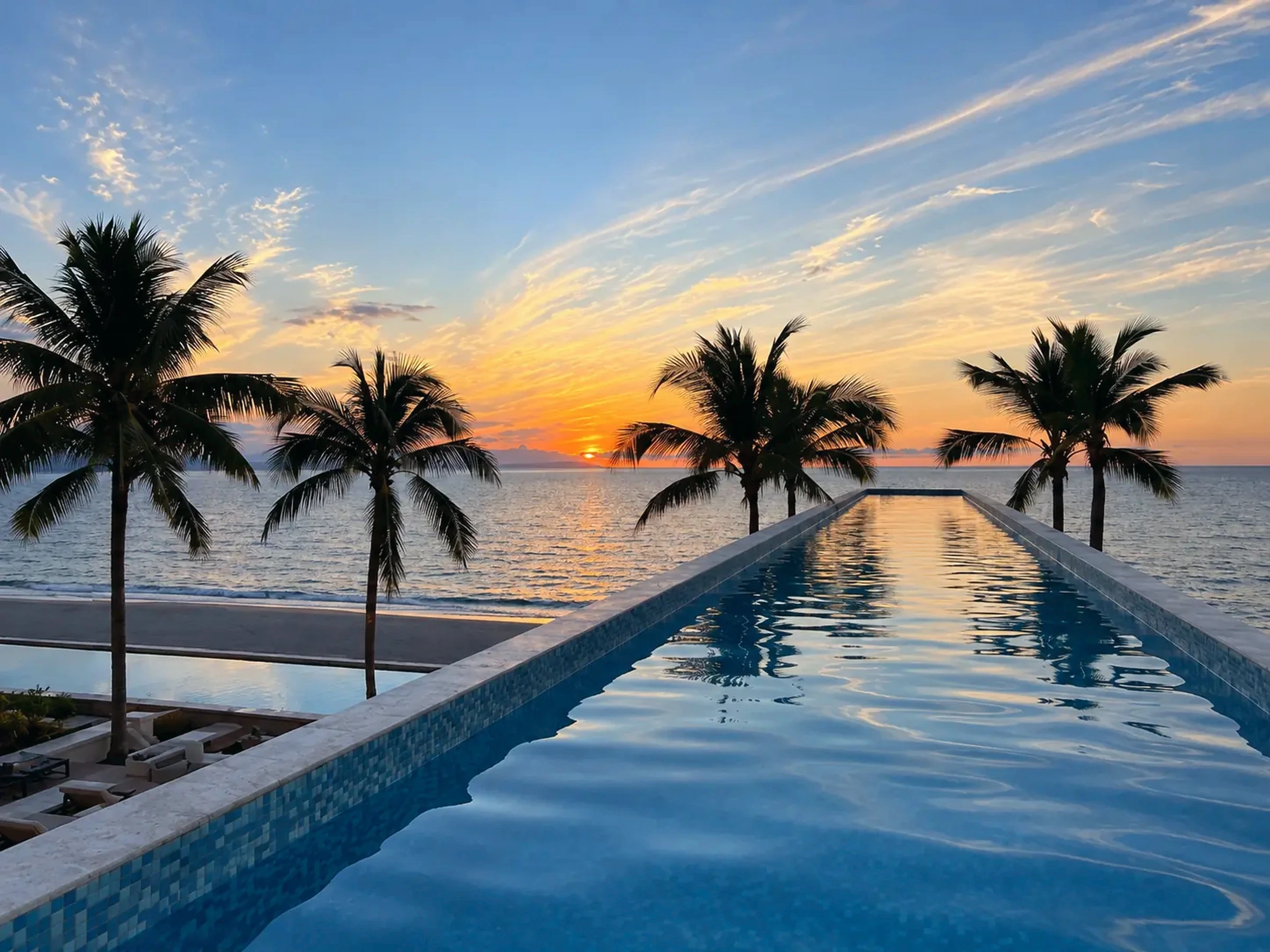 Oceanfront pool framed by palms at sunset
